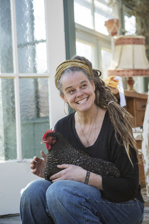 Nico Simmeth mit lachendem Gesicht hält ein schwarzes Huhn auf dem Schoß in der Orangerie