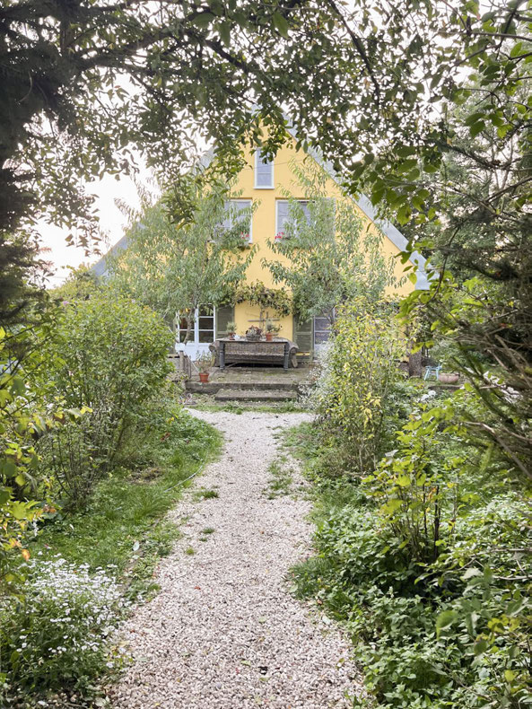 Gelbes Hofgebäude am Ende eines kiesbedeckten Gartenwegs